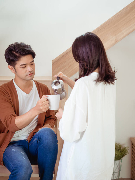 若いアジアの女性と男は手にコーヒーのカップと一緒に家で一緒に時間を過ごしています. - 写真・画像