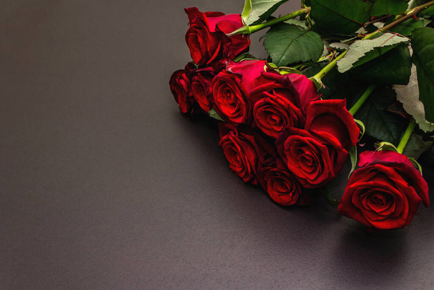 Букет свежих бургундских роз на черном каменном бетонном фоне. Ароматные красные цветы, концепция подарка на День Святого Валентина, свадьбу или день рождения - Фото, изображение