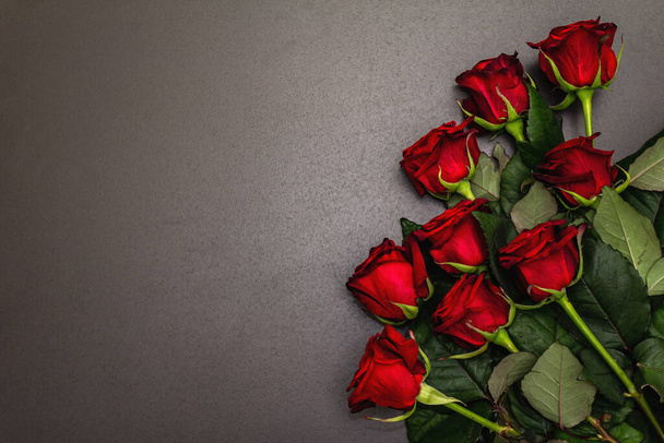 Букет свежих бургундских роз на черном каменном бетонном фоне. Ароматные красные цветы, концепция подарка на День Святого Валентина, свадьбу или день рождения - Фото, изображение