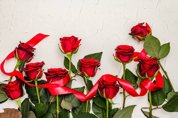Rosas borgonhas frescas com fita de cetim vermelho em um fundo de massa branca. Flores vermelhas perfumadas, conceito de presente para o Dia dos Namorados, casamento ou aniversário - Foto, Imagem