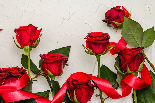 Frische weinrote Rosen mit rotem Satinband auf weißem Spachtelgrund. Duftende rote Blumen, Geschenkkonzept für Valentinstag, Hochzeit oder Geburtstag - Foto, Bild