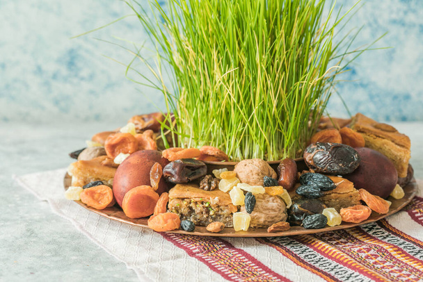 Novruz traditional tray with green wheat grass semeni or sabzi, sweets and dry fruits pakhlava on white background. Spring equinox, Azerbaijan copy space - Photo, Image