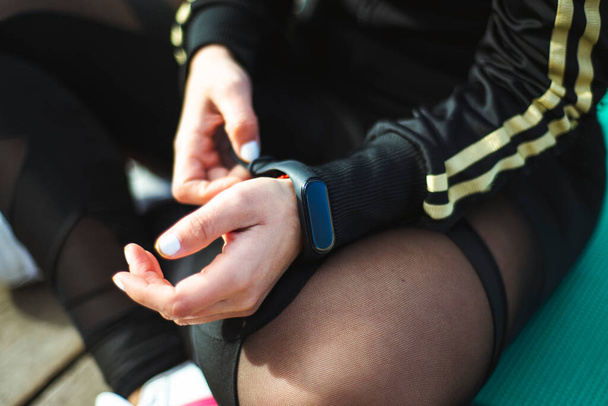 Young fit woman checking smart watch while sitting on yoga mat - Fotografie, Obrázek