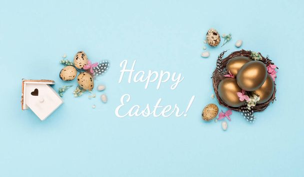 Festive Easter holiday greeting card background. Easter Decoration with golden eggs, quail feathers, dried flowers on blue background. Happy Easter card concept. Copy space, top view. - Photo, Image