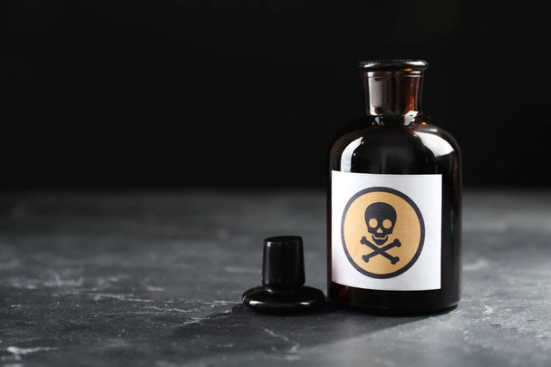 Open glass bottle of poison with warning sign on black table. Space for text - Fotó, kép