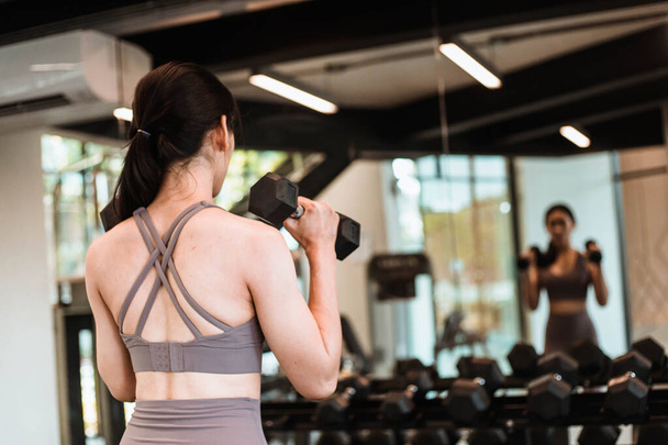 back of Young beautiful slim woman doing exercises with dumbbell in gym - Photo, Image