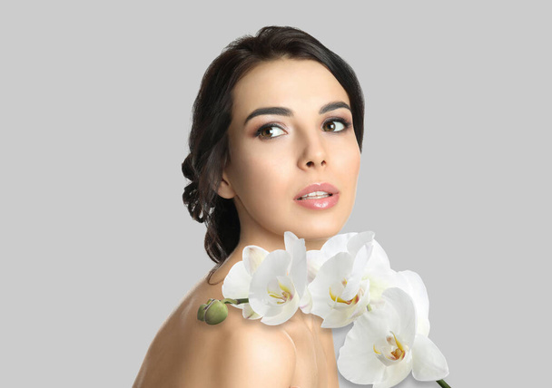 Beautiful young woman and orchid flowers on light background. Spa portrait - Φωτογραφία, εικόνα