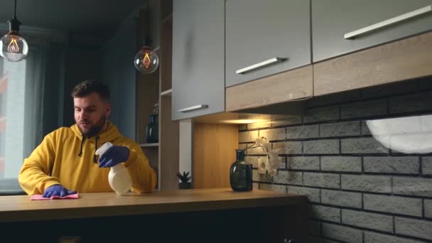 Kaukaski mężczyzna używa rękawic i wycierać podczas sprzątania domu specjalnym sprayem - Materiał filmowy, wideo
