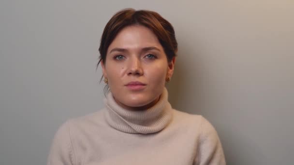 Kaukázusi nő beszél a kamera előtt egy szürke falon meleg pulóvert visel. - Felvétel, videó