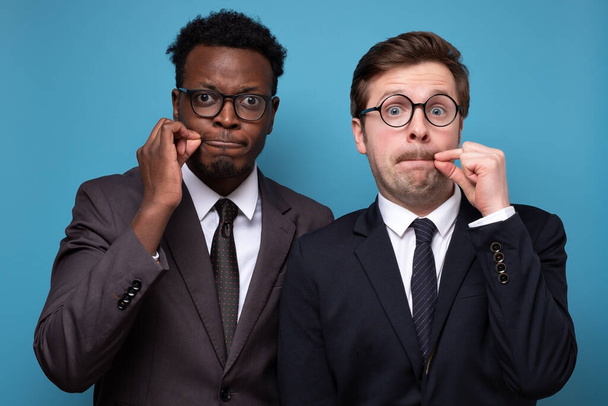 Due uomini africani e caucasici chiudono bocca come zip con le dita - Foto, immagini