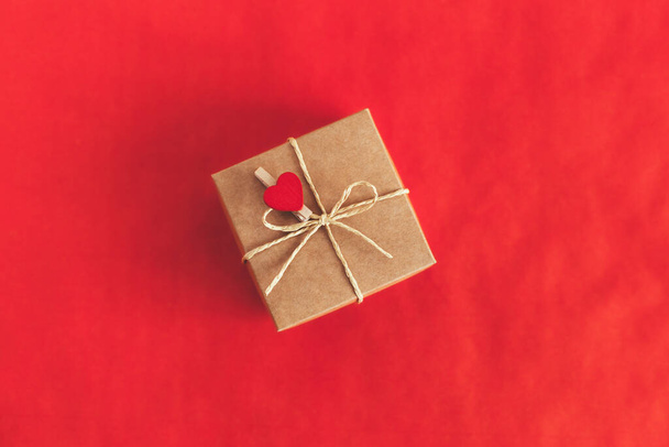 Caja de regalo artesanal con corazón rojo sobre fondo rojo. Concepto de vacaciones para el día de San Valentín. Lugar para el texto. Puesta plana. - Foto, Imagen