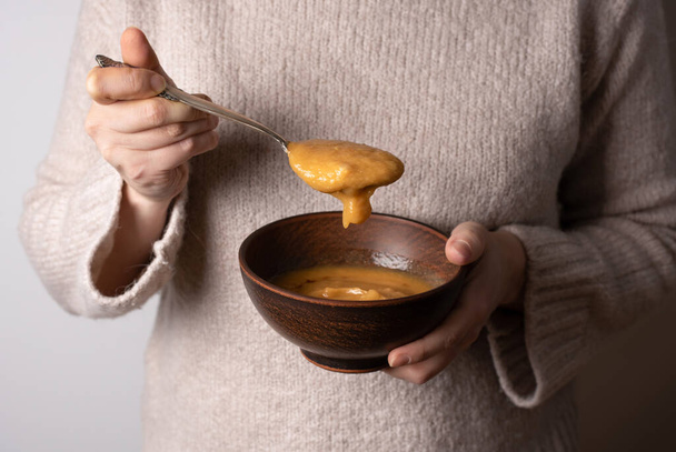 Las manos femeninas sosteniendo un tazón de sopa de crema de lentejas rojas vegetarianas y una cuchara llena de sopa, de cerca. - Foto, imagen