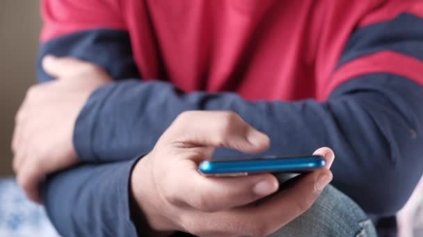 mladý muž sedí na posteli pomocí chytrého telefonu  - Záběry, video