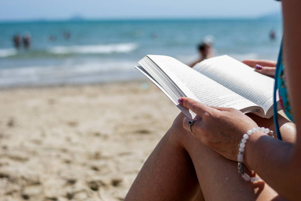 Woman reading a book on the beach, blurred background. Summer leisure on the beach. - Valokuva, kuva