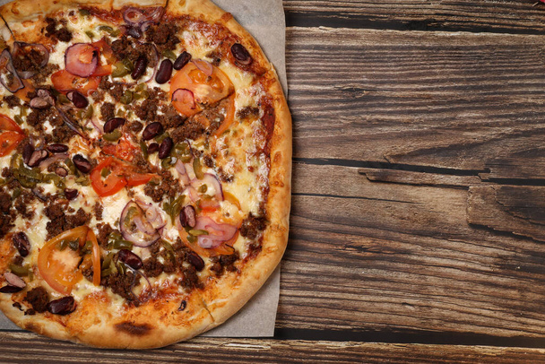 Top view of fresh baked pizza with meat and vegetables on a wooden table. Pizza delivery. Take away. - Photo, Image