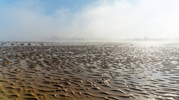 A panorama landscape of fog lifting over an endless wadden sea beach at low tide - Foto, afbeelding