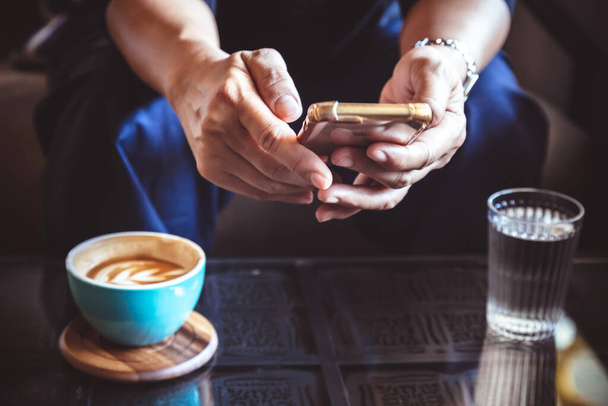biznesmen korzystający ze smartfona do czytania wiadomości inwestycyjnych i odpowiedzi e-mail w celu potwierdzenia spotkania w kawiarni. człowiek pijący kawę latte przed pójściem do pracy w poniedziałek rano. rocznik zdjęcie i styl filmu - Zdjęcie, obraz