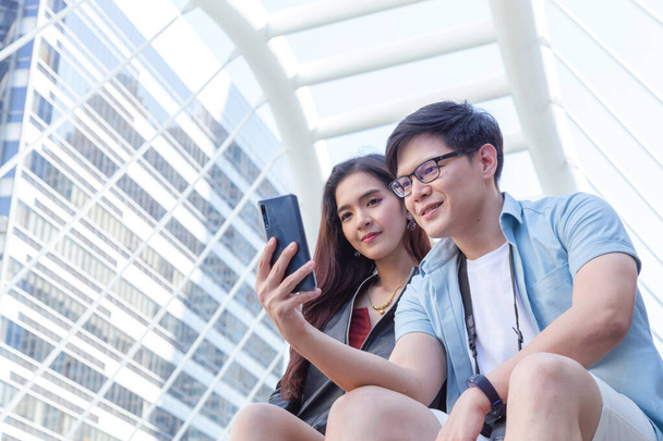 young asian man and woman couple lover traveler using smartphone or mobile phone to searching hotel, shopping center and transportation guide information on application. lifestyle and travel concept. - Photo, Image