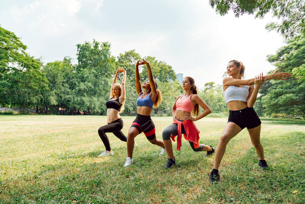 šťastný zdravé čtyři krásné mladé teenagery žena školení a protahování pro zahřívání před cvičením v parku. fitness, sport, přátelství a zdravý životní styl. - Fotografie, Obrázek