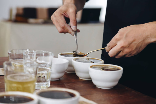 профессиональный Q Grader готовится к проверке и проверке качества кофе и обезжиренный от кофейного основания из керамической чашки на столе. фото в стиле кино. - Фото, изображение