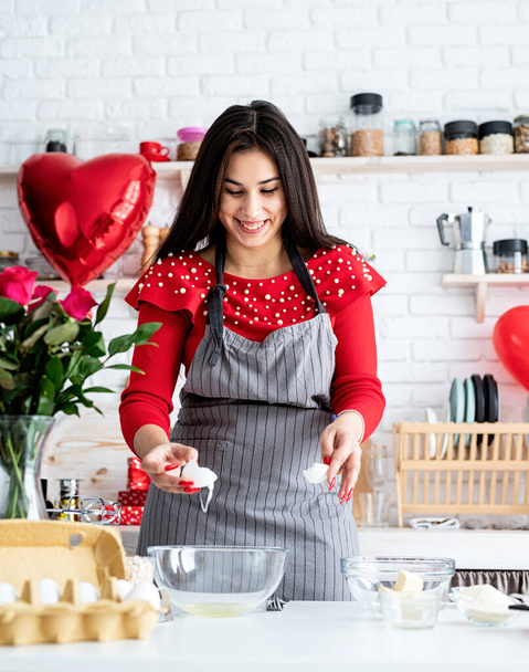 Día de San Valentín. Mujer en vestido rojo y delantal gris haciendo galletas de San Valentín en la cocina - Foto, imagen