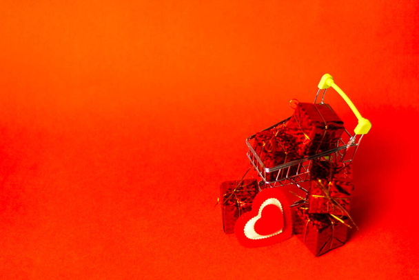 Shopping trolley with gift box, love hearts and cope space on red background. St. Valentine's Day shopping and sale. - Photo, Image