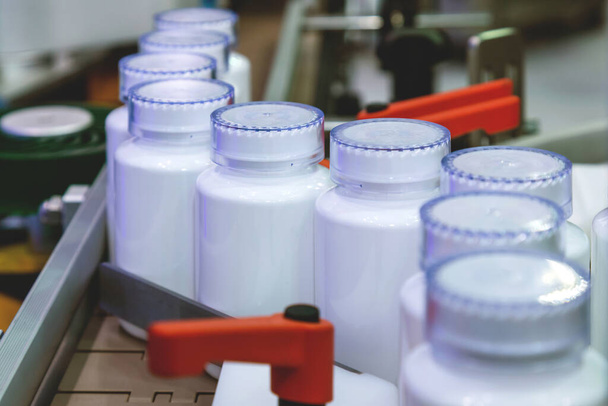 Tıbbi fabrikadaki dolum makinesinin üretim hattındaki beyaz ilaç plastik şişesi. Seçici odaklanma. İlaç imalatı ve sanayi konsepti. - Fotoğraf, Görsel