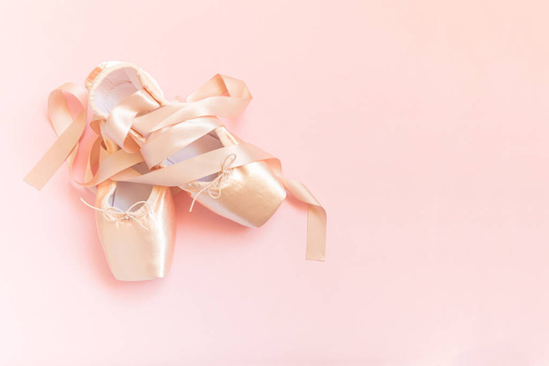 Nouvelles chaussures de ballet beige pastel avec ruban de satin isolé sur fond rose. Chaussures à pointe classique ballerine pour l'entraînement de danse. Concept de l'école de ballet. Vue du dessus espace de copie plat laïc - Photo, image