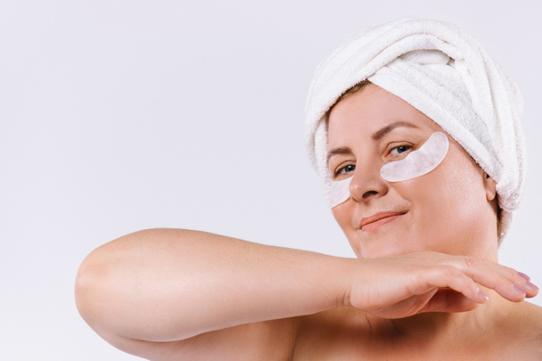 Natural older woman. With a towel on the head and pads under the eyes. Home skin care concept on white background. - Photo, Image