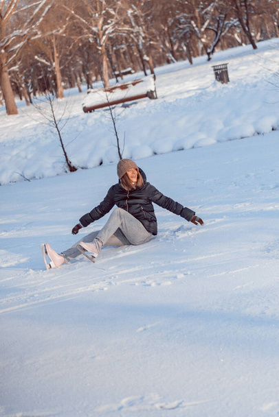 Young woman learns ice skating, falls, sits on the snow, winter sports, snow, winter fun. - Foto, afbeelding