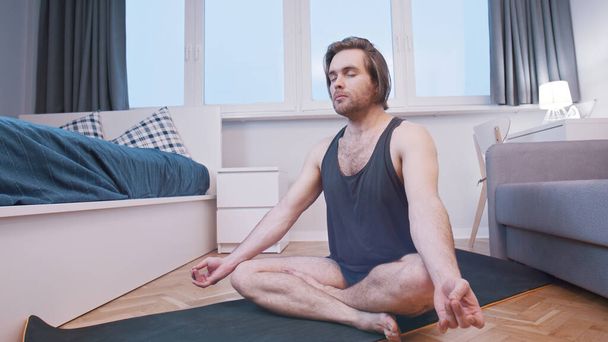 Young calm man meditating in his bedroom. Wellbeing concept - Photo, Image
