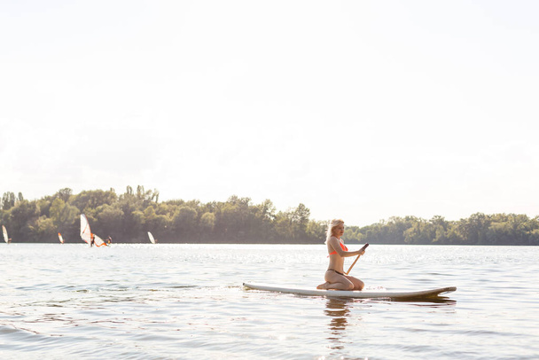 vrouw met een peddel op het schoolbord. benen van een slank meisje op stand up paddle board. - Foto, afbeelding