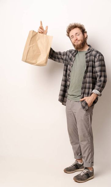 Man in plaid shirt holding brown paper bag isolated on white background. Delivery concept. Paper bag for takeaway food. Courier with a bag on white background - Photo, image
