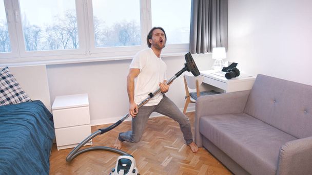 Young caucasian man with a vacuum cleaner dancing at home - Foto, Bild