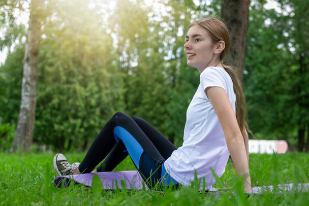 Chica adolescente haciendo yoga en el parque. Adolescente descansando después de actividades deportivas - Foto, imagen