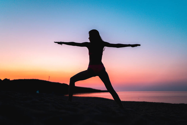 Silhueta de mulher fazendo ioga na praia ao pôr do sol durante a hora de ouro. - Foto, Imagem