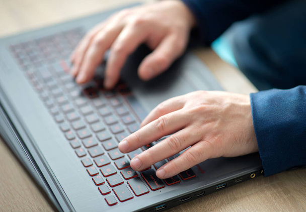 Τα χέρια ενός ανθρώπου πληκτρολογούν σε ένα πληκτρολόγιο laptop. Ένας άντρας σε μια δουλειά γραφείου γράφει σε ένα λάπτοπ. Επιλεκτική εστίαση - Φωτογραφία, εικόνα
