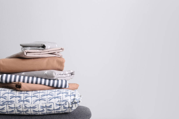 Stack of clean bed linen and pillow on light grey background. Space for text - Valokuva, kuva