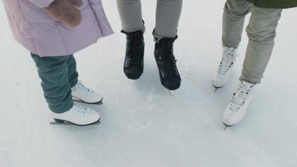 Primo piano ad angolo alto di gambe irriconoscibili che indossano pattini da ghiaccio fermi sulla pista di pattinaggio all'aperto - Filmati, video