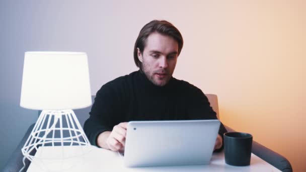 彼のアパートでノートパソコンでビデオ会議をしている若い白人男性 - 映像、動画
