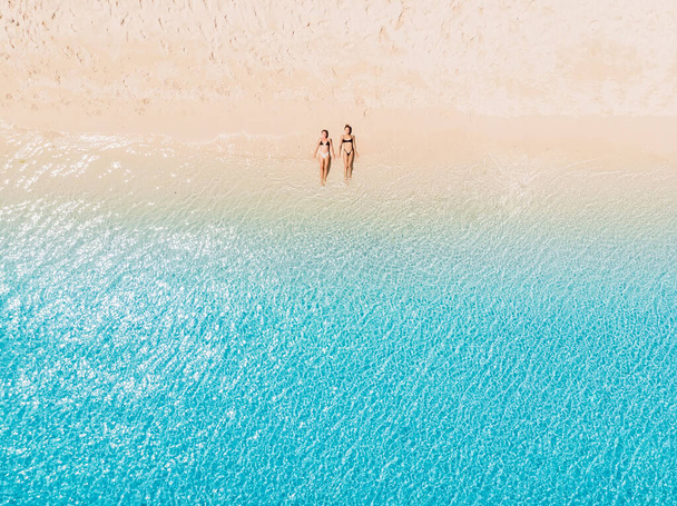 Pareja de mujeres relajándose en la playa paradisíaca con mar azul. Vista aérea - Foto, Imagen