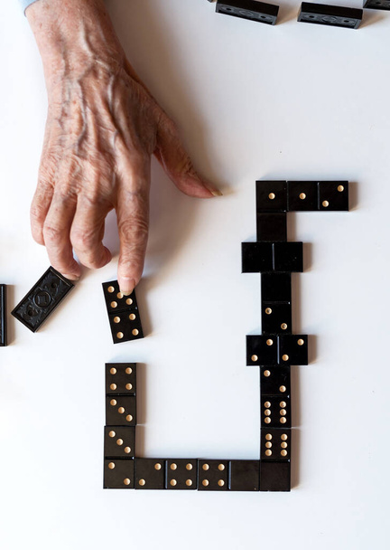 Rodzinna rozrywka dla zabawy rekreacyjnej gry domino. Ręka starszej kobiety kładzie domino na stole. - Zdjęcie, obraz