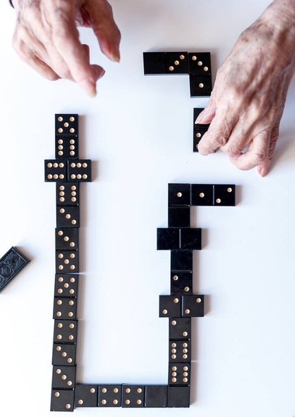 Family entertainment for a fun leisure game of dominoes. The hand of an elderly woman puts a domino on the table. - Foto, imagen