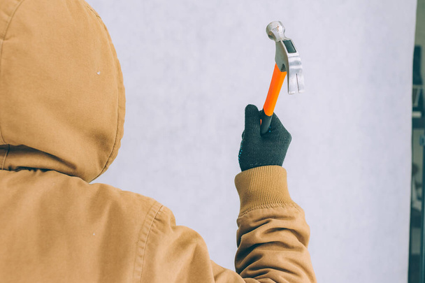 Um homem segura um martelo de construção em suas mãos em um fundo leve - Foto, Imagem