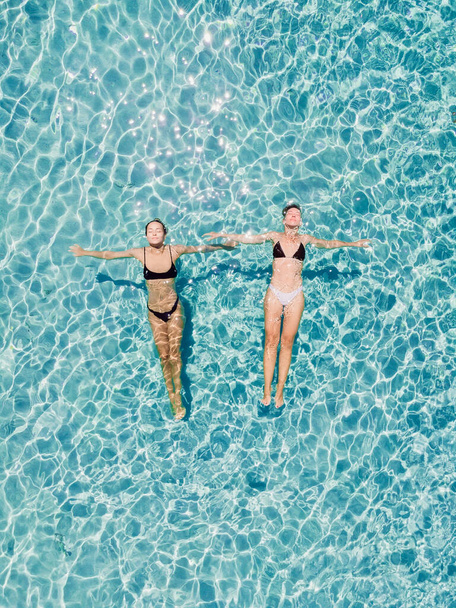 Een paar vrouwen drijvend in een doorzichtige blauwe oceaan. Luchtzicht - Foto, afbeelding