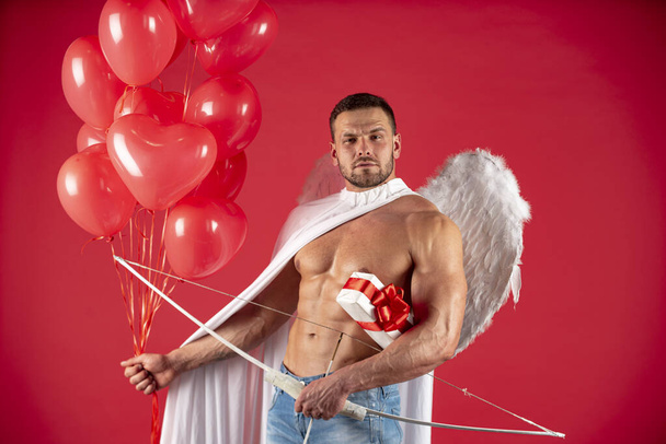 Valentines Day male. Sexy angel man with angels wings. Arrow of love, cupid, amour. February 14. Isolated on red. - Фото, изображение
