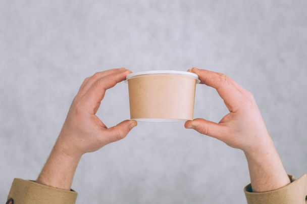 A man holds a mock-up of a paper cup for soup, coffee and tea on a light background - Foto, immagini
