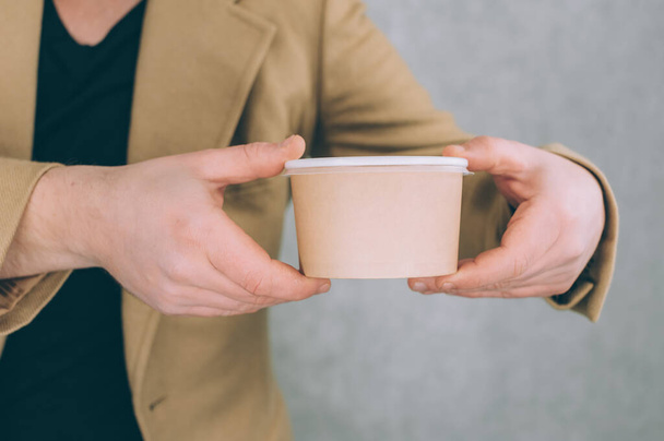 A man holds a mock-up of a paper cup for soup, coffee and tea on a light background - Foto, Imagem