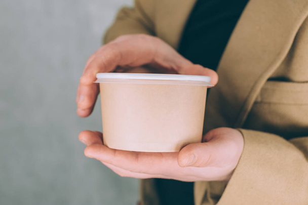 A man holds a mock-up of a paper cup for soup, coffee and tea on a light background - Photo, image