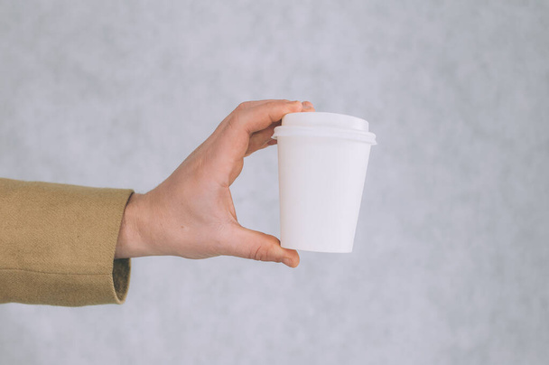 A man holds a mock-up of a paper cup for coffee and tea on a light background - Foto, immagini